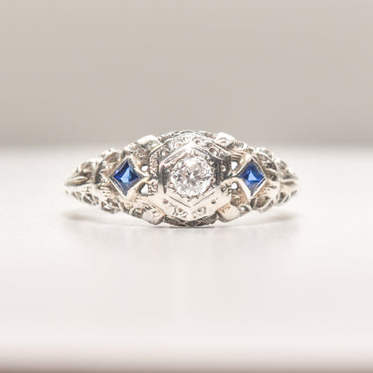 Art Deco 18K white gold engagement ring with diamond center and synthetic sapphire accents, size 6.25, with intricate filigree design.