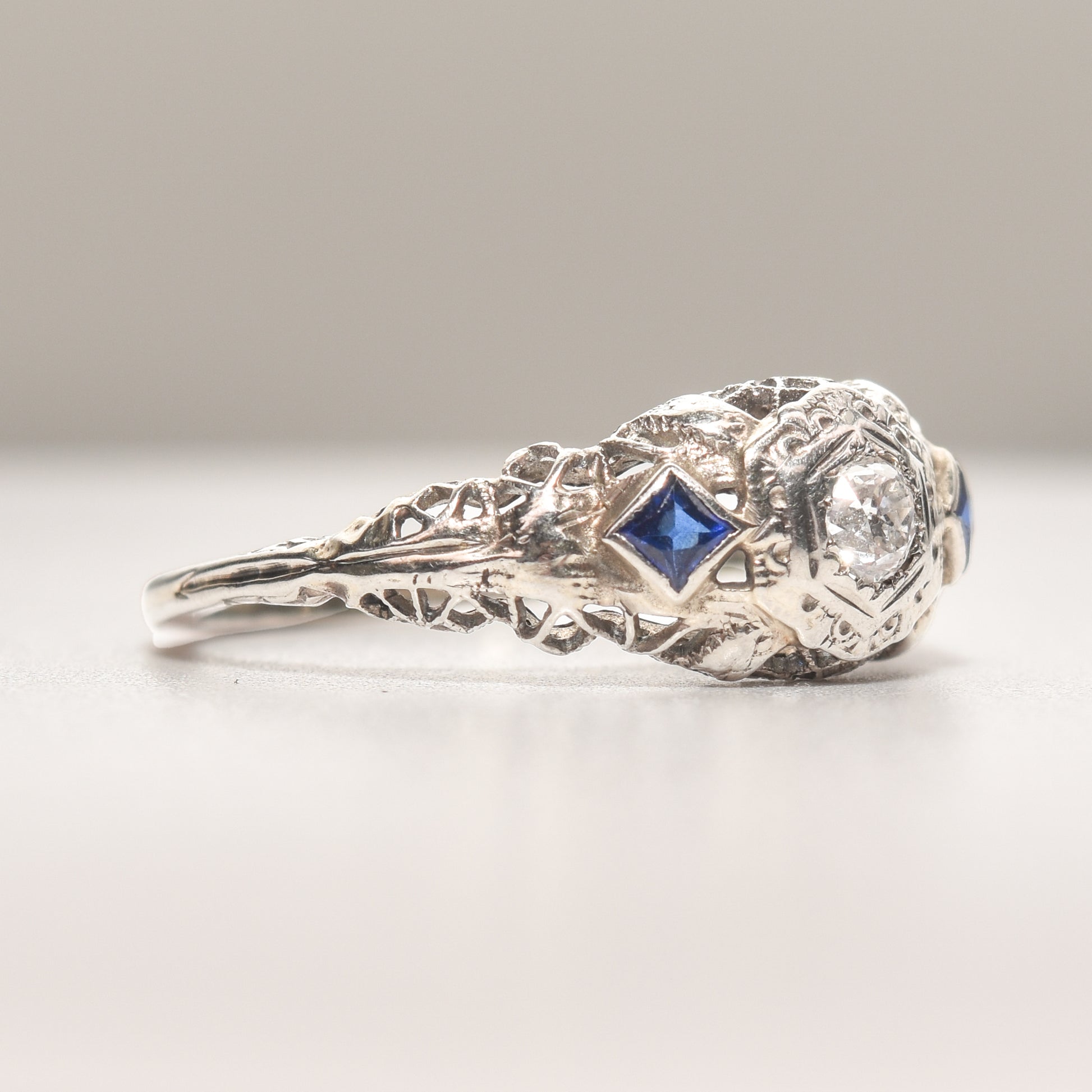 Art Deco 18K white gold diamond and sapphire filigree engagement ring with natural diamonds and synthetic sapphires on a size 6.25 US band, intricate vintage design.