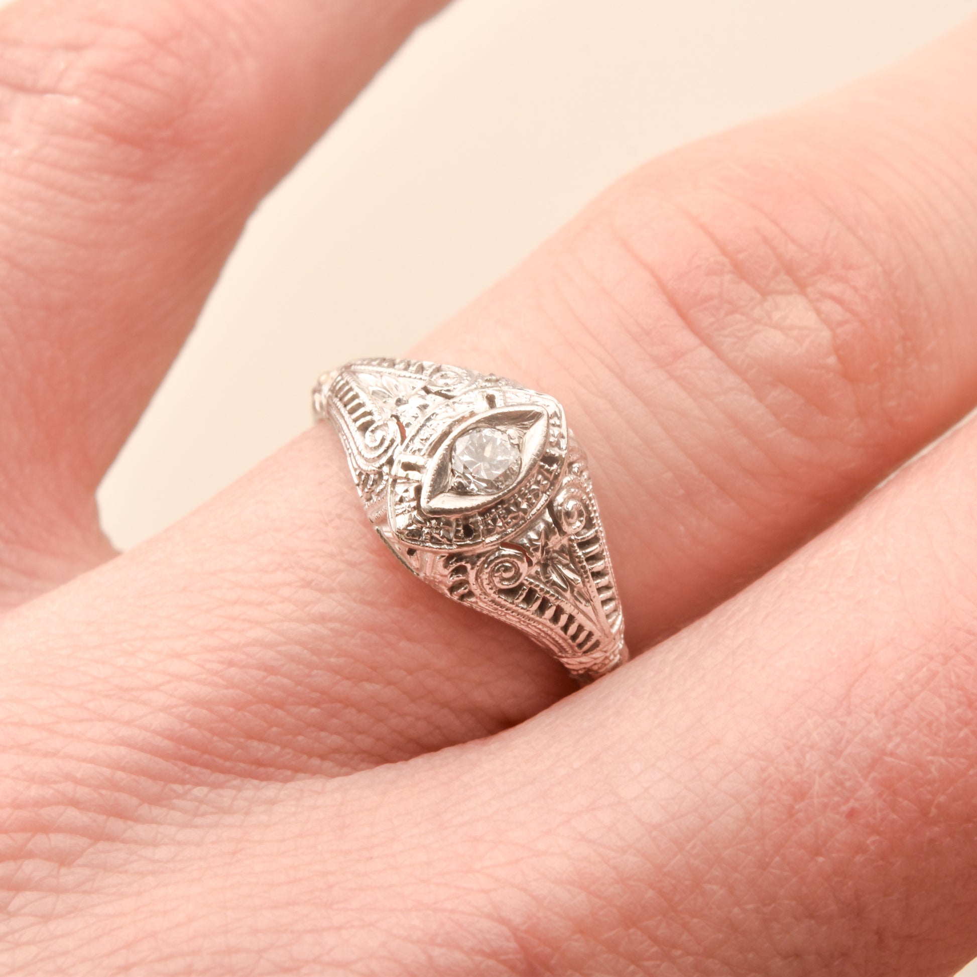 Art Deco 18K filigree diamond solitaire ring with 0.08 CT brilliant diamond, size 6.25 US, on a person's finger.