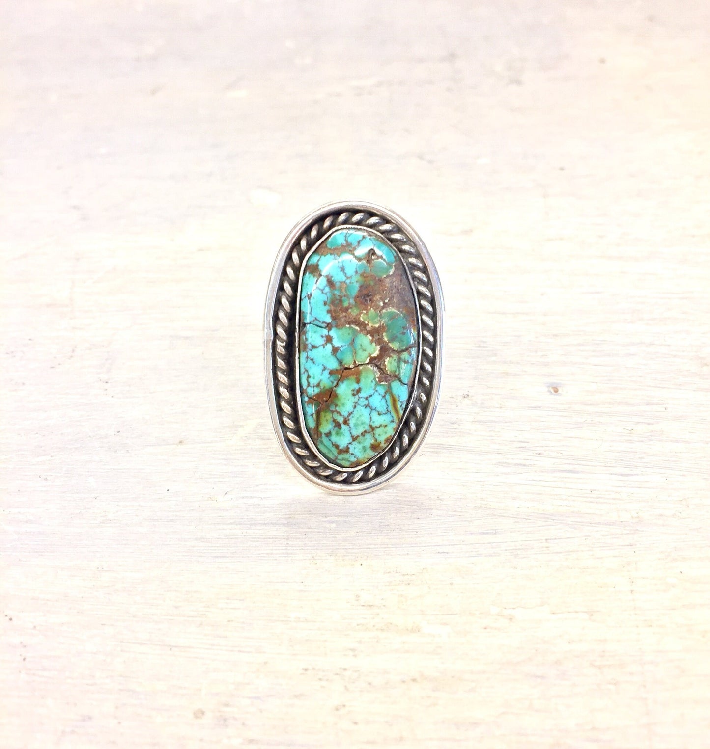 Vintage sterling silver ring featuring a large oval turquoise stone with matrix pattern, set in a twisted rope style bezel on a textured silver band.