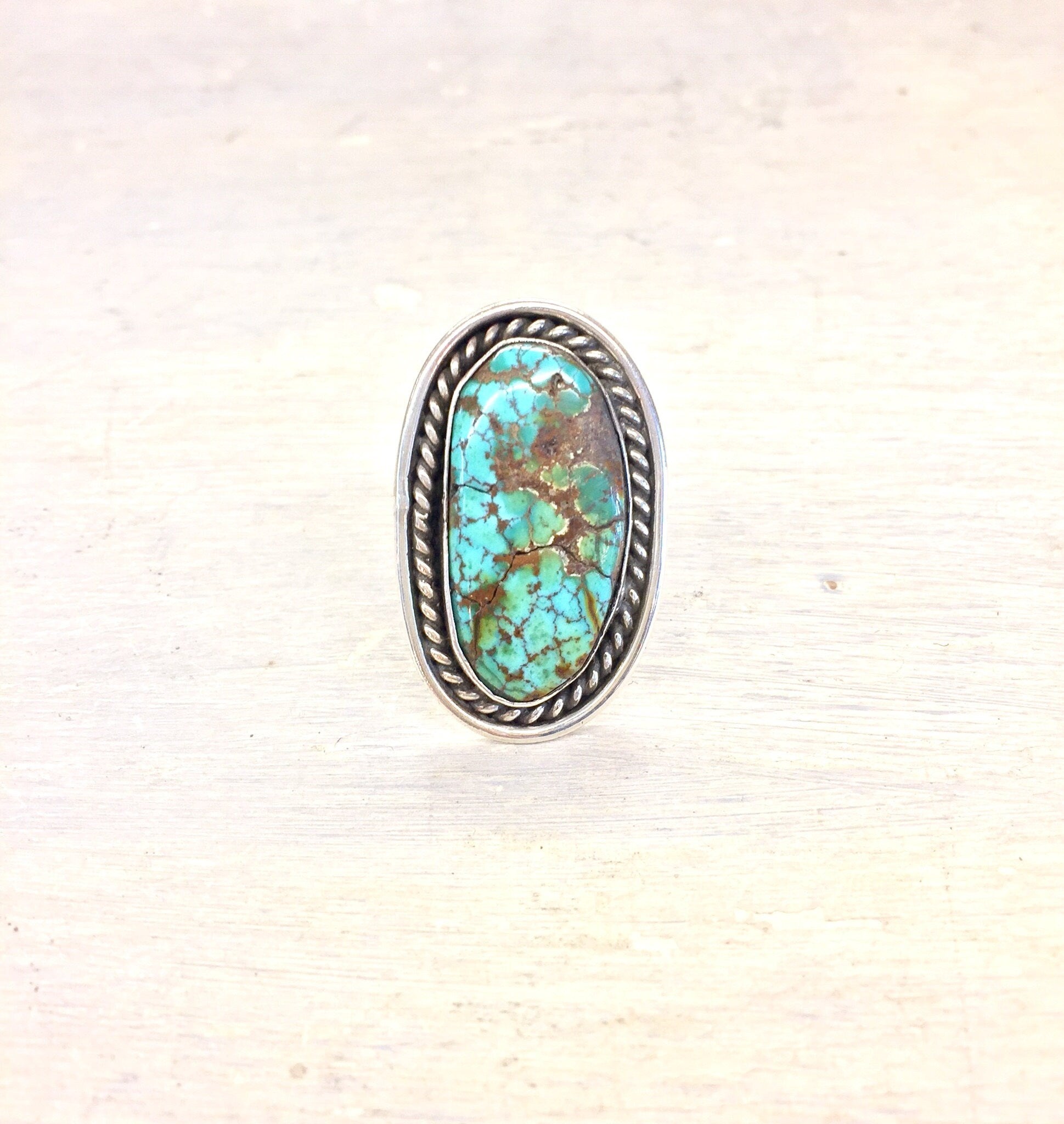 Vintage sterling silver ring featuring a large oval turquoise stone with matrix pattern, set in a twisted rope style bezel on a textured silver band.