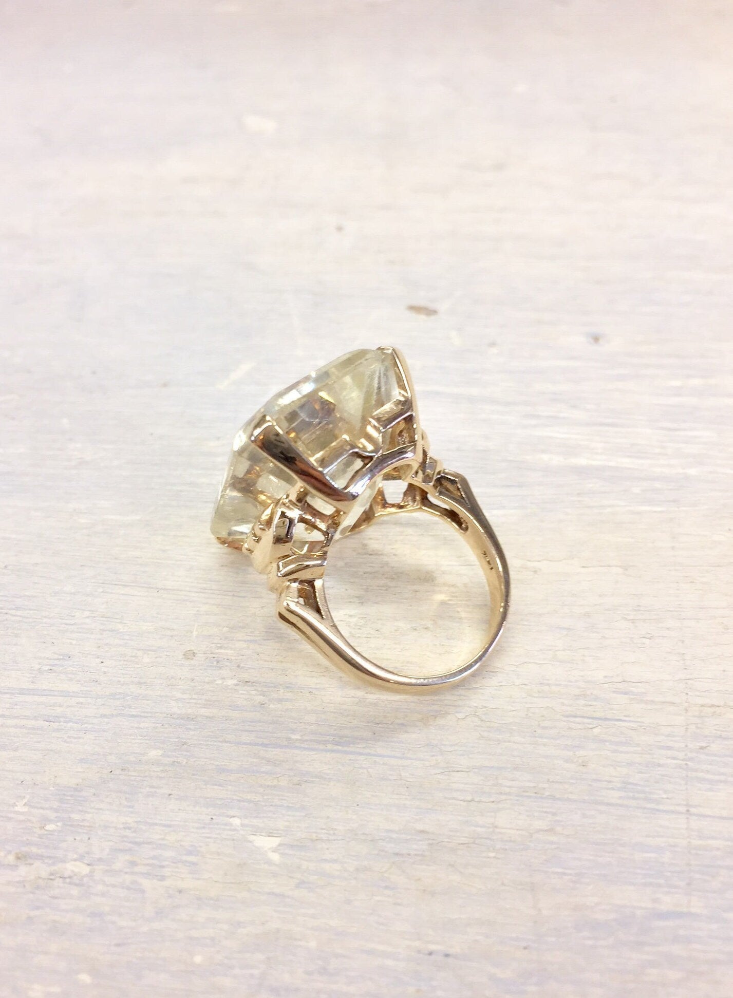 14 karat yellow gold vintage cocktail ring with large faceted gemstone on light wooden surface, viewed from above.