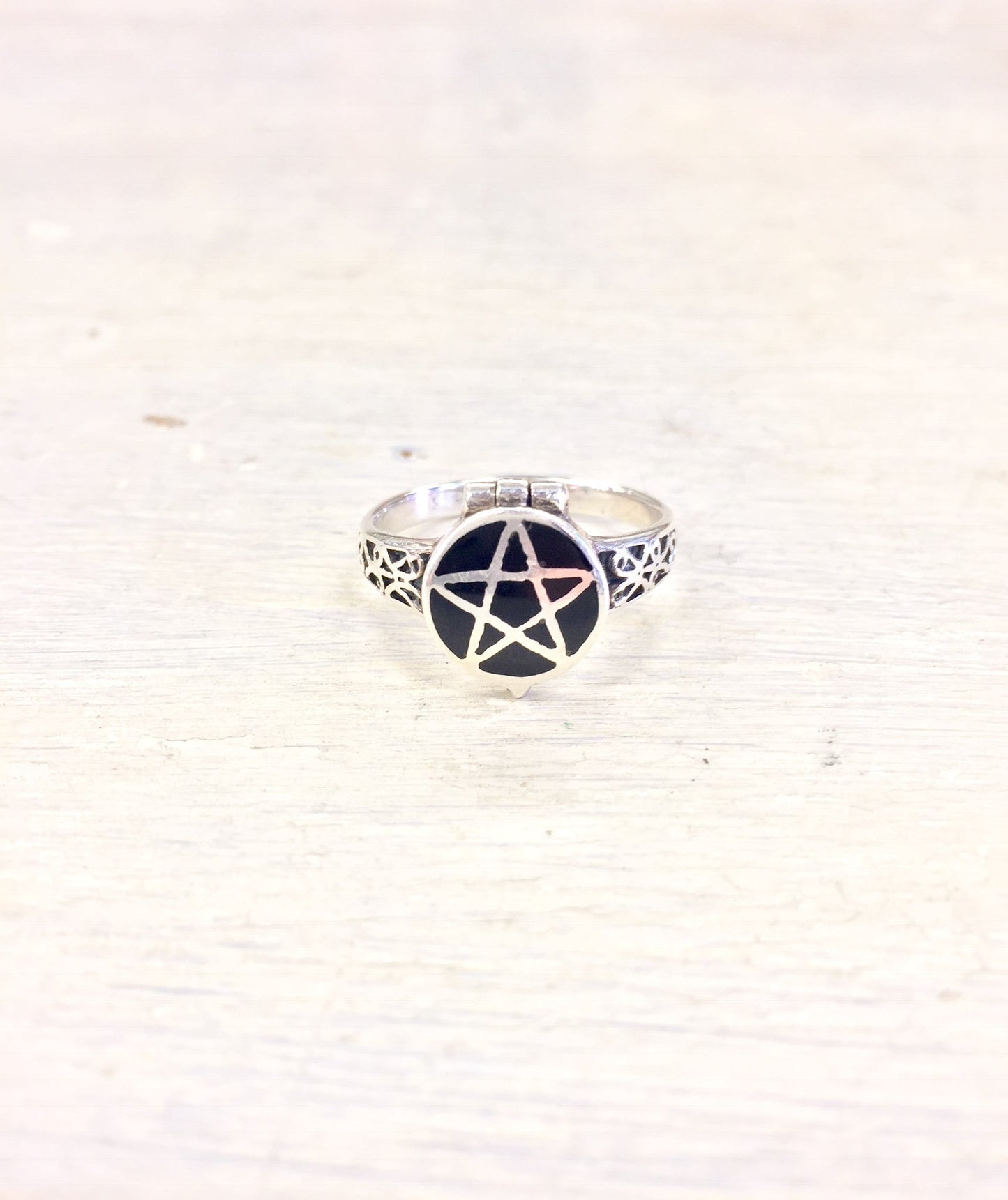 Sterling silver pentagram poison ring against white fabric background