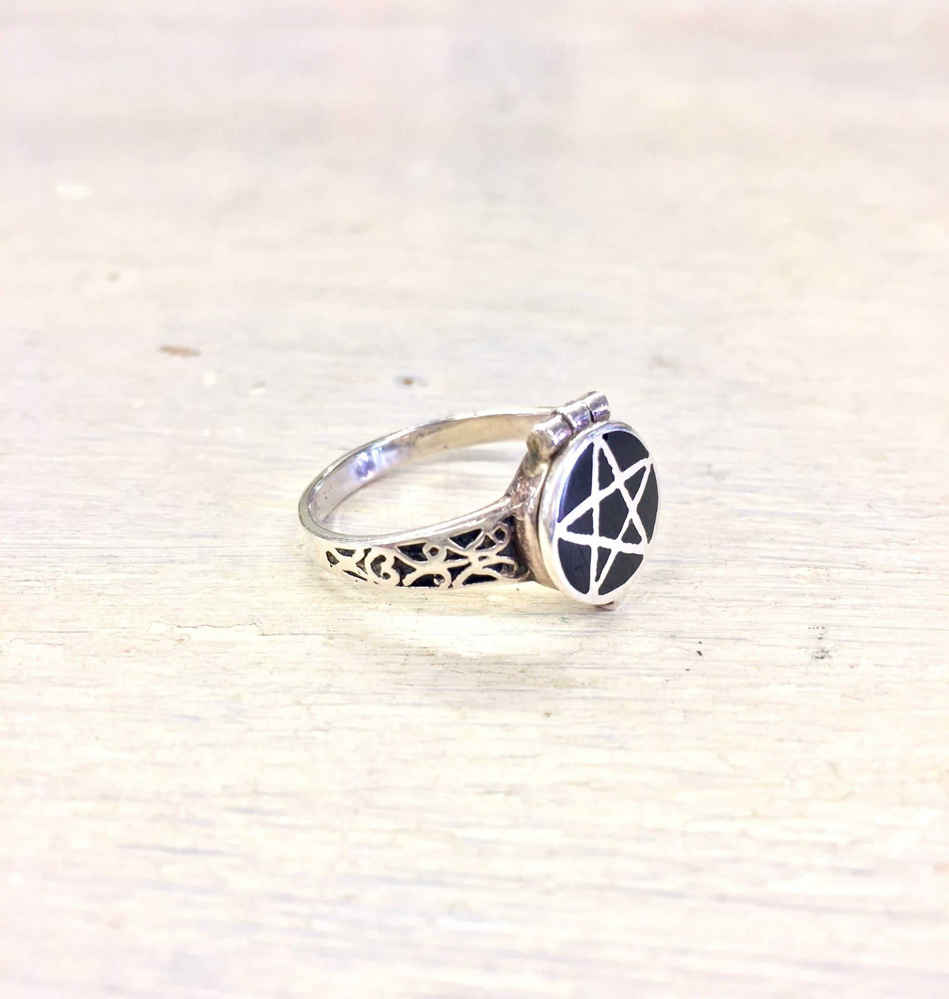 Vintage sterling silver poison ring with intricate gothic pentagram design on a textured wooden surface, elegant antique statement jewelry piece.