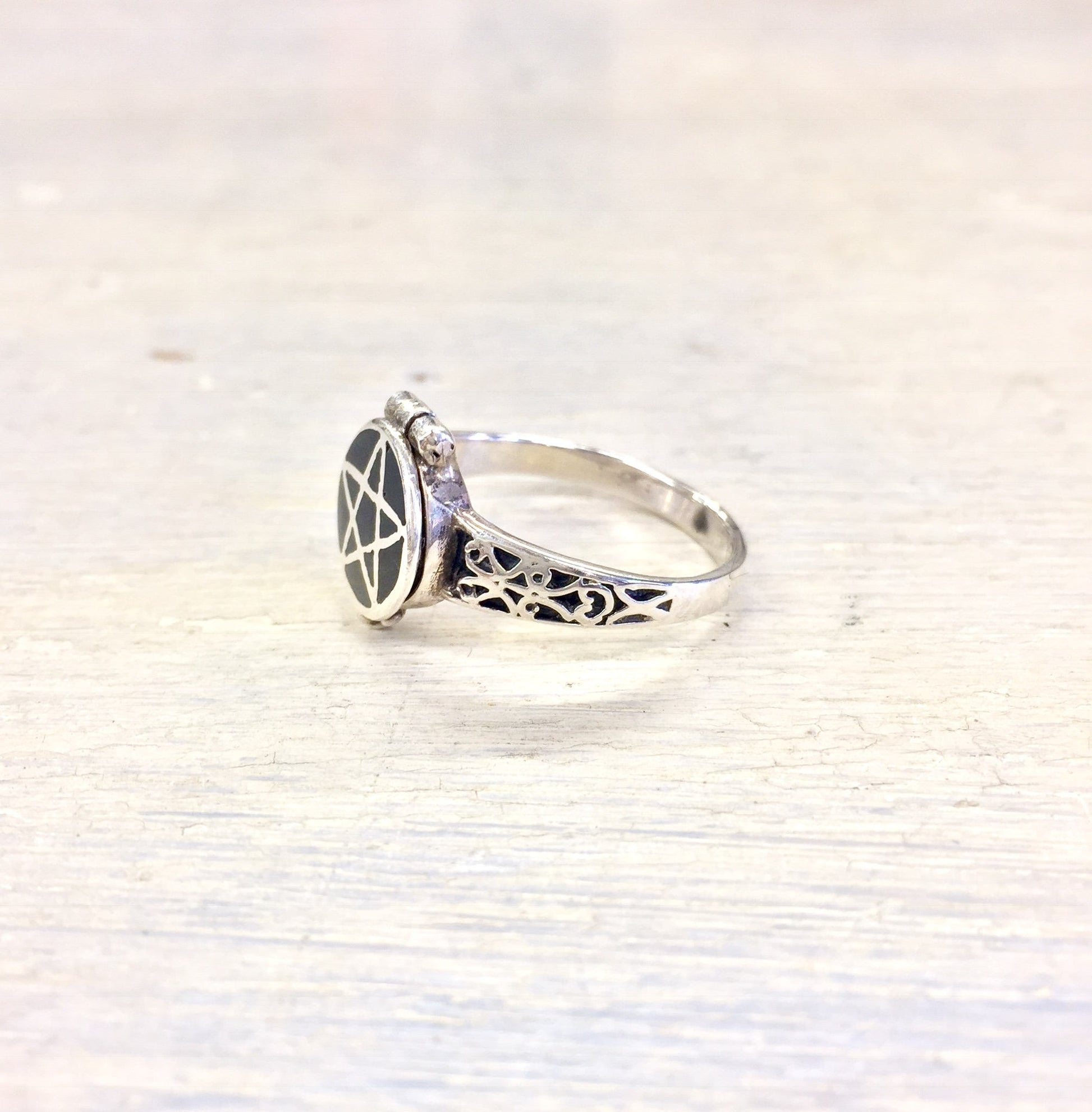 Vintage sterling silver poison ring with intricate gothic pentagram design and hidden compartment, displayed on a light wooden surface.