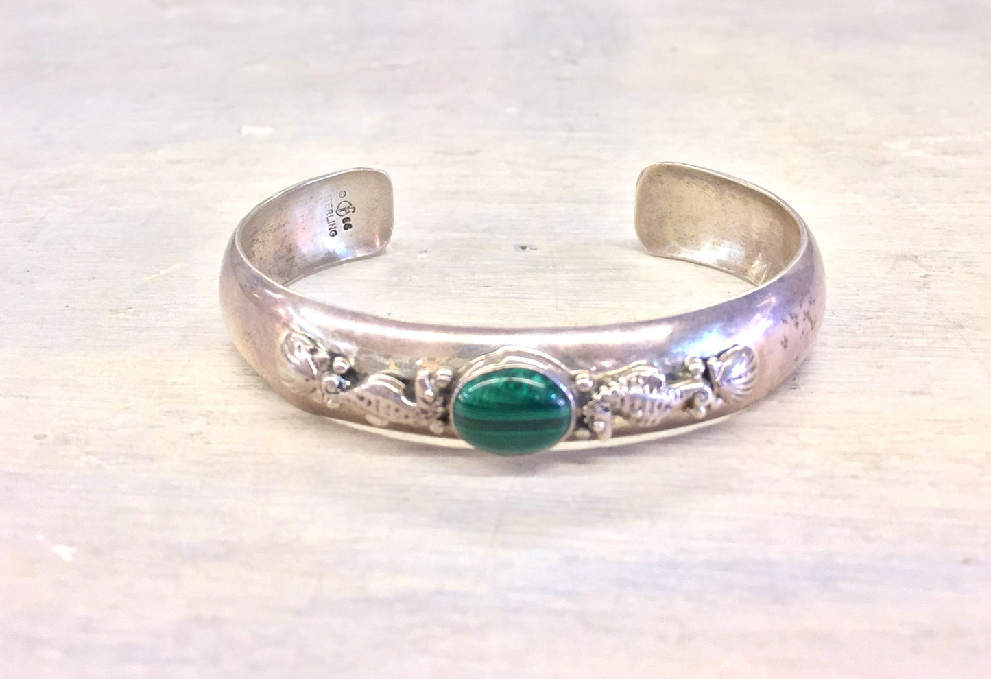 Vintage sterling silver cuff bracelet featuring intricate seahorse design and vibrant green malachite cabochon centerpiece.