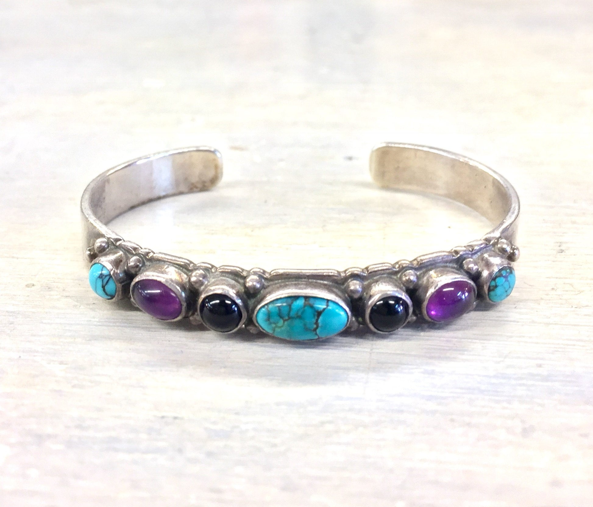 Sterling silver cuff bracelet with turquoise, purple, and black onyx gemstones in a vintage style.