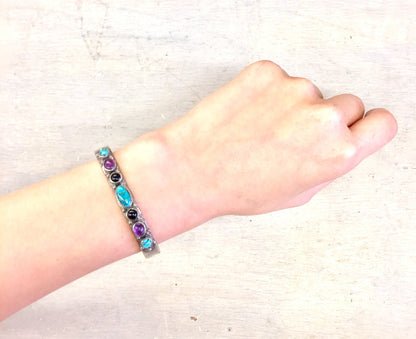 Vintage silver cuff bracelet with turquoise, onyx and purple stones on woman's wrist against textured background