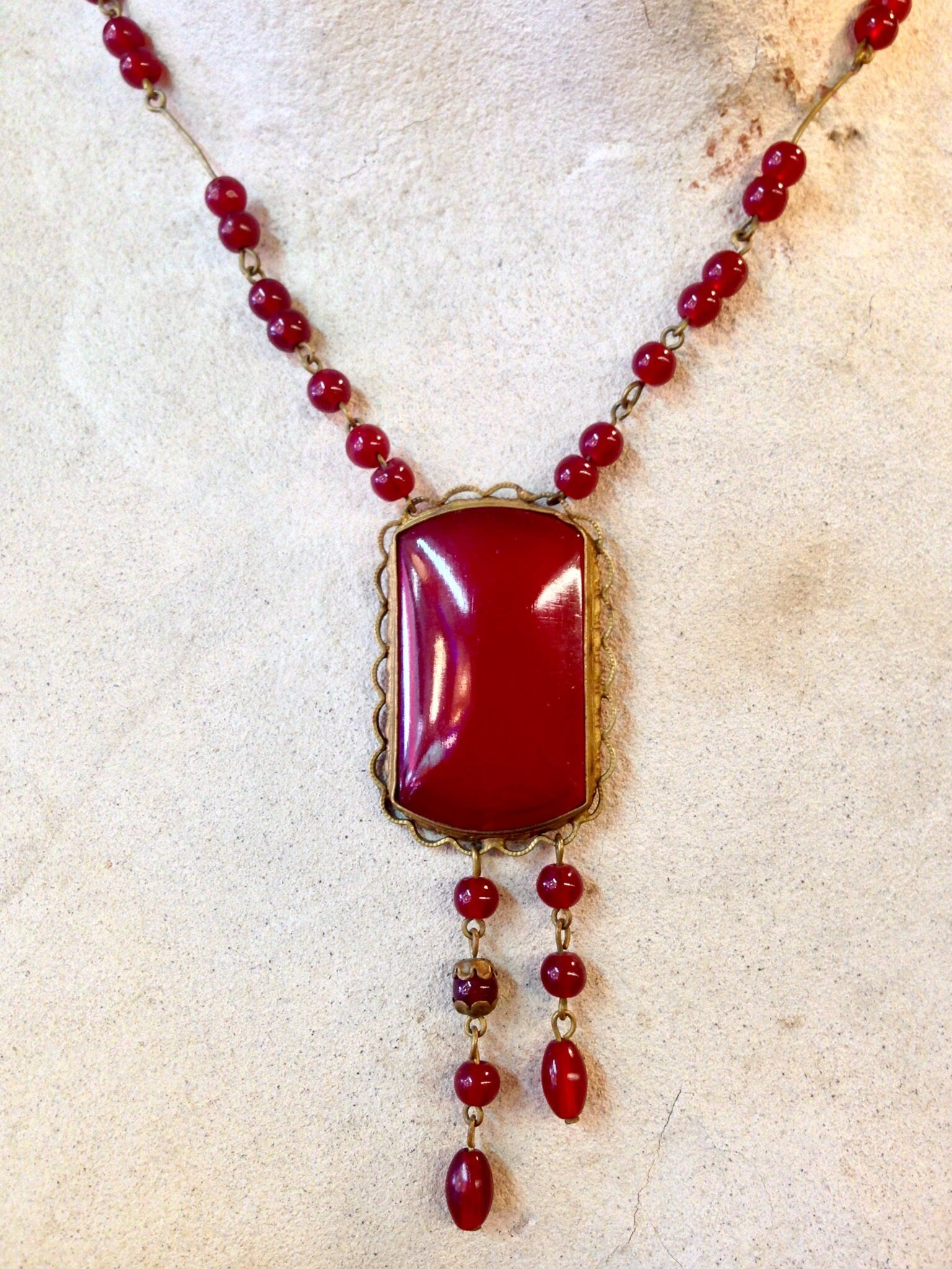 Vintage red beaded necklace with gothic-style pendant and dangling beads on an antique paper background.