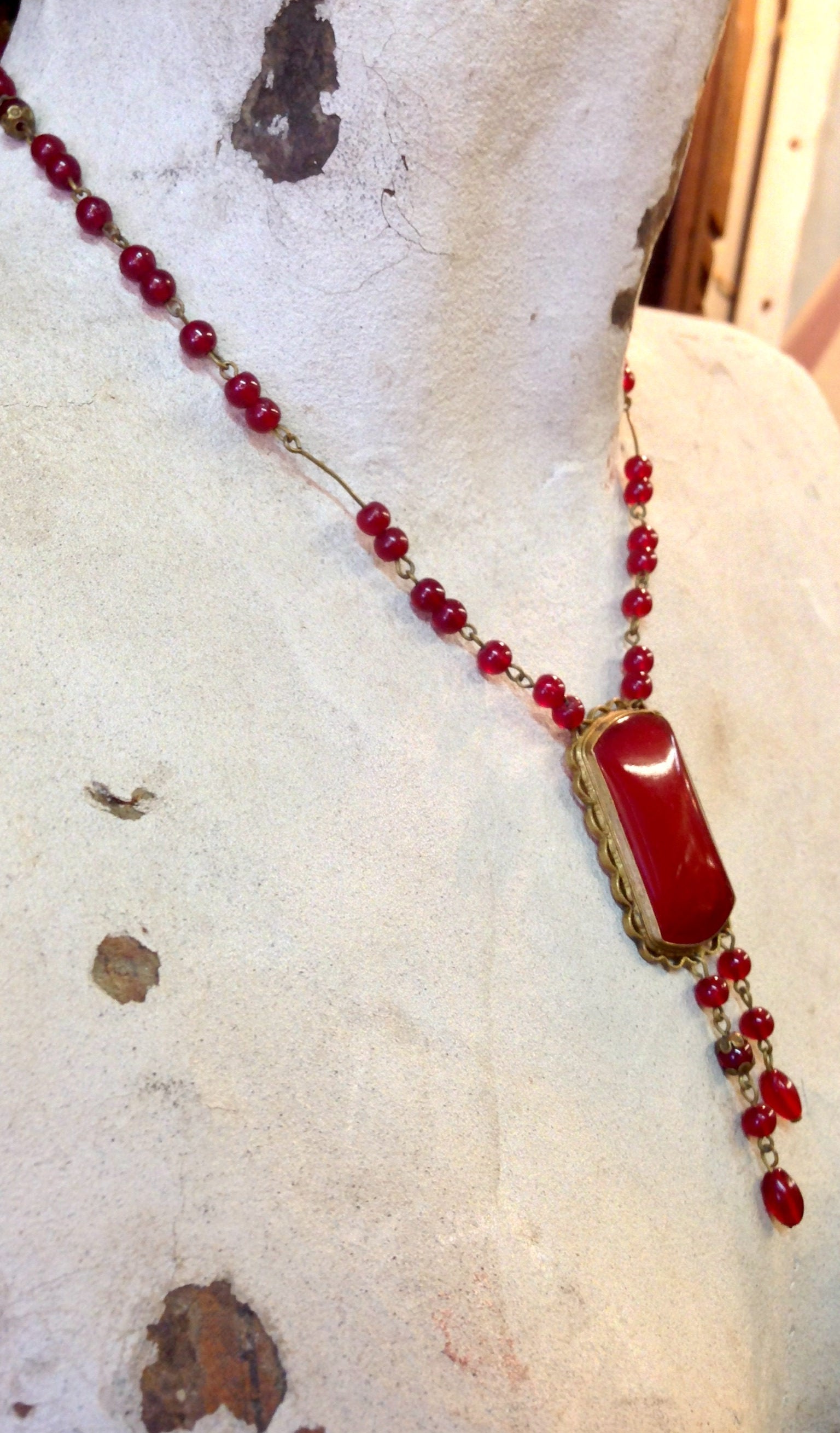 Vintage red beaded necklace with rectangular pendant on snowy background with dried leaves