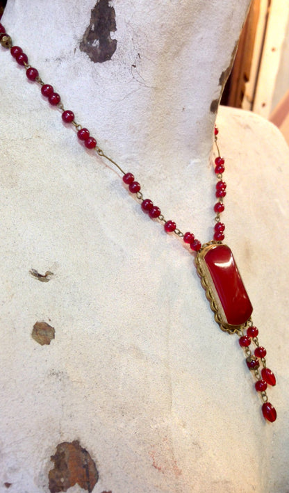 Vintage red beaded necklace with rectangular pendant on snowy background with dried leaves