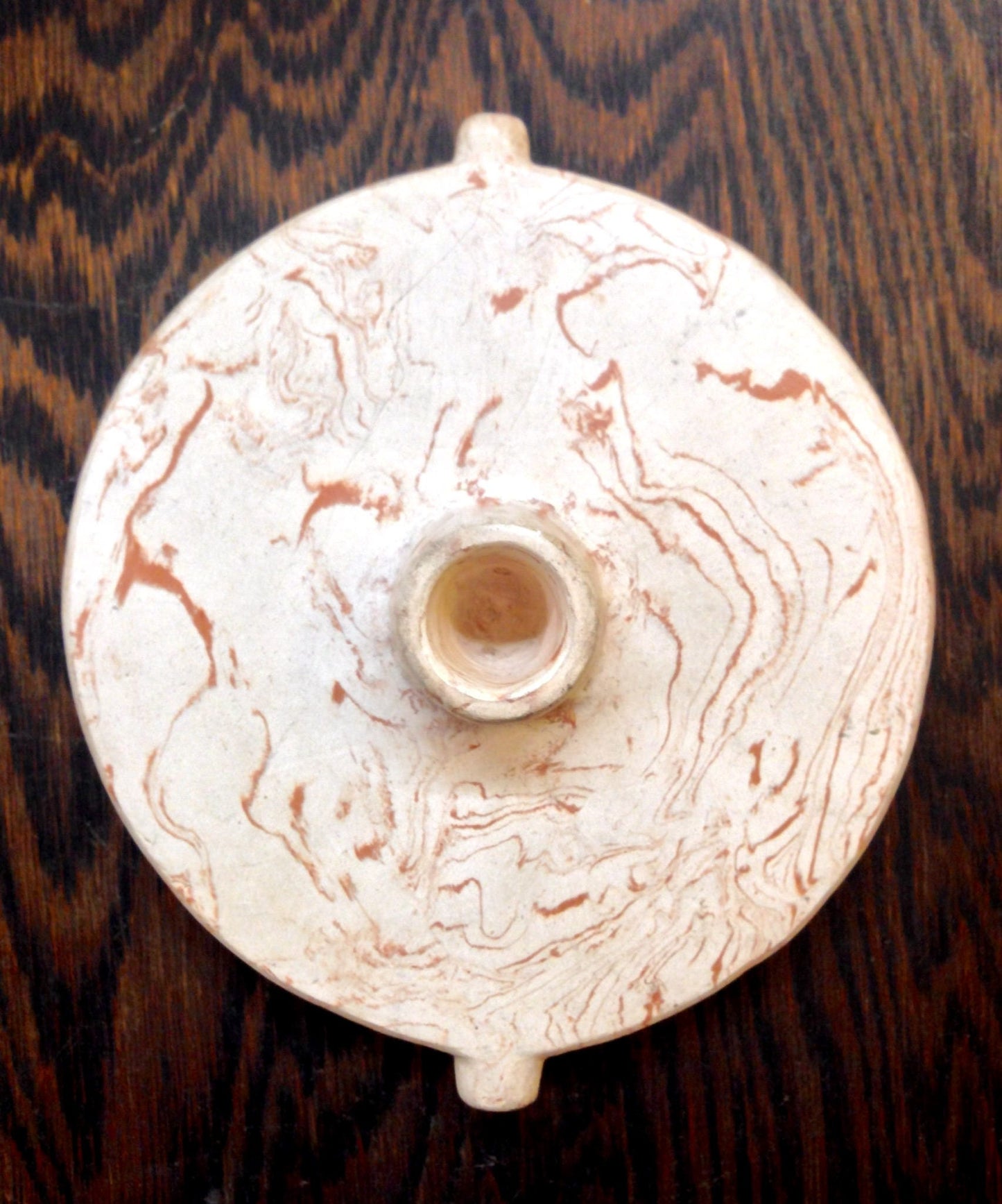 Antique white ceramic tobacco pipe with swirled abstract patterns on a dark wooden surface, viewed from above.