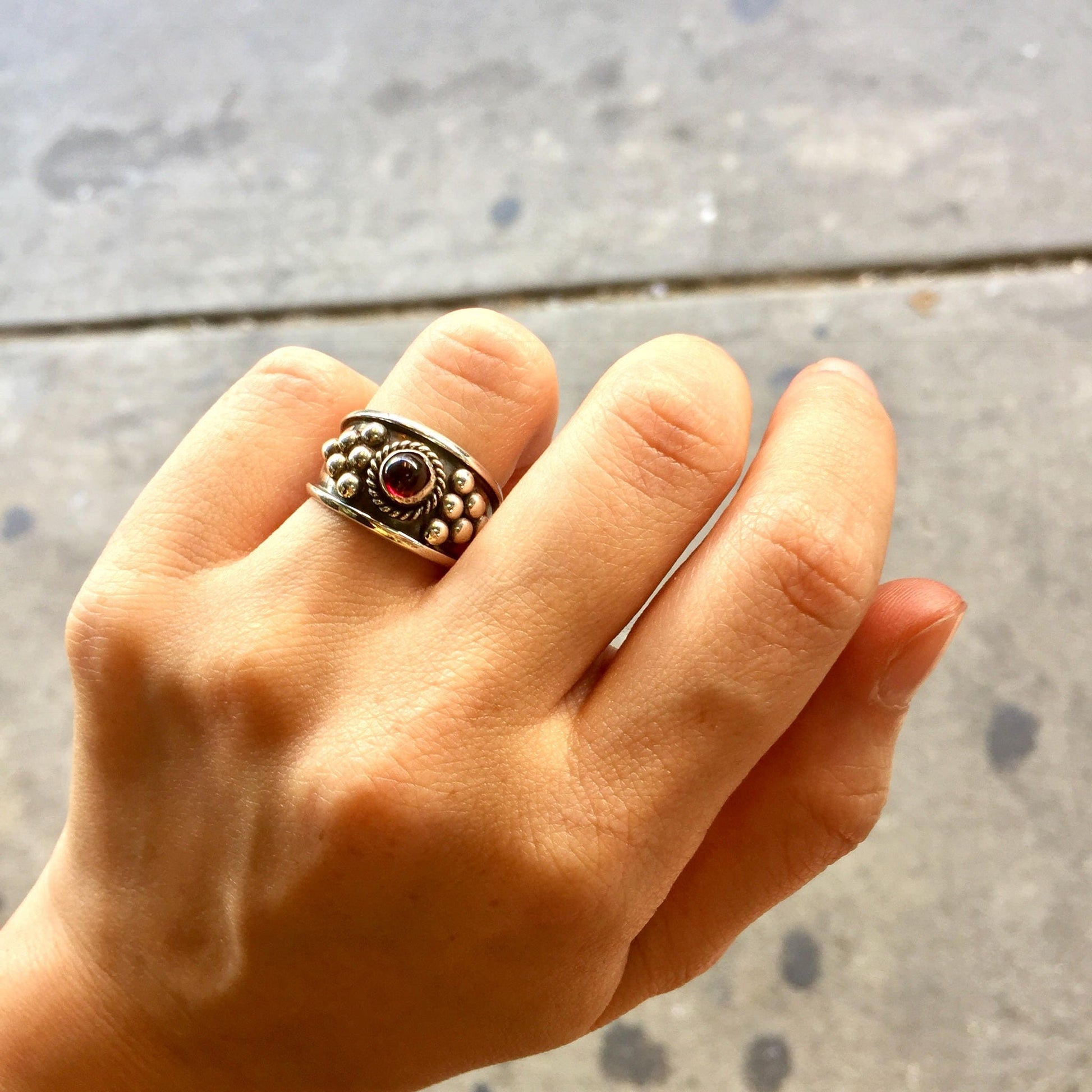 Vintage sterling silver ring with red garnet gemstone in ornate gothic Celtic design, shown on hand against concrete background.