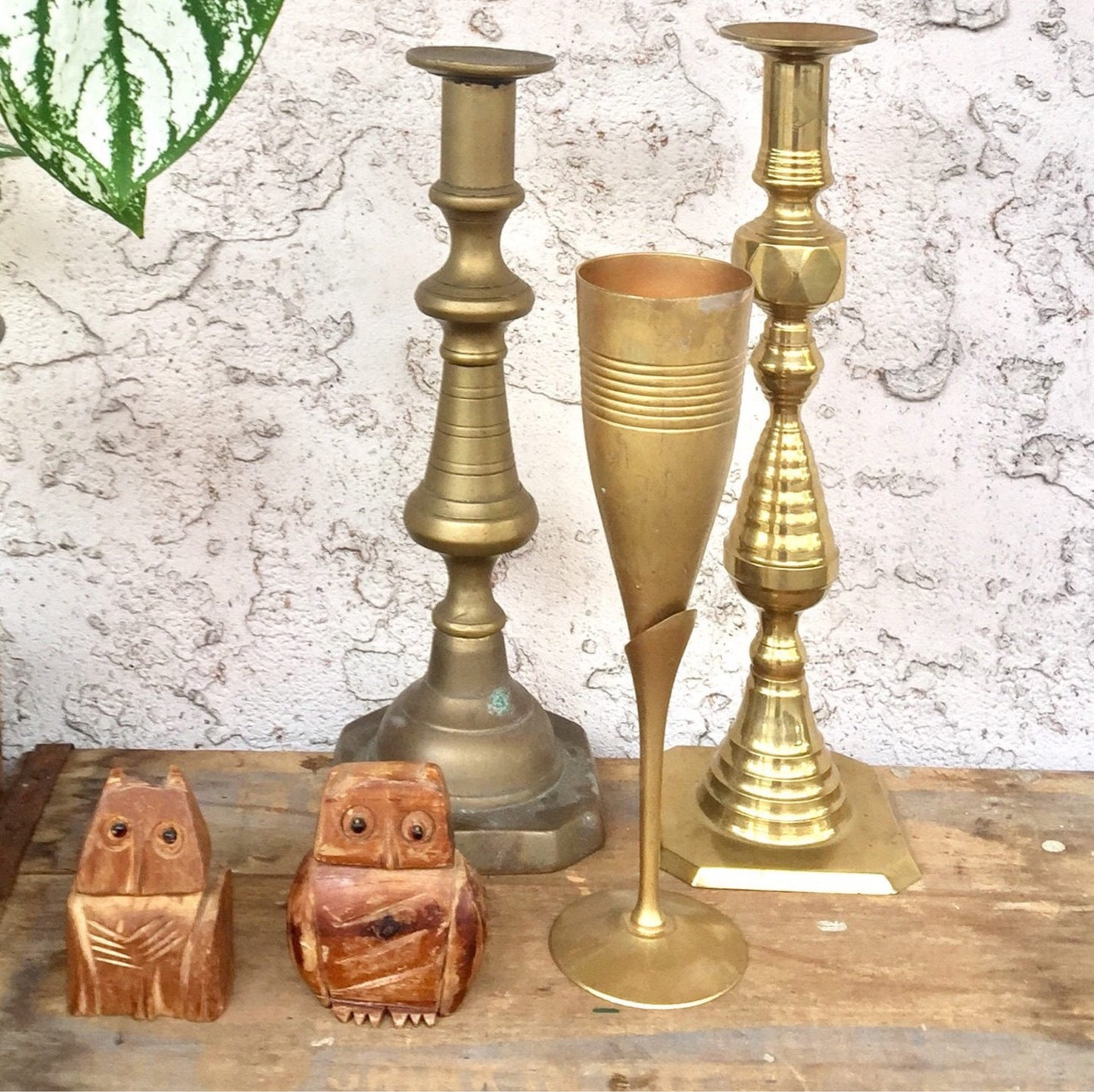 Vintage brass candlesticks and wood carved owl figurines on weathered wood surface.