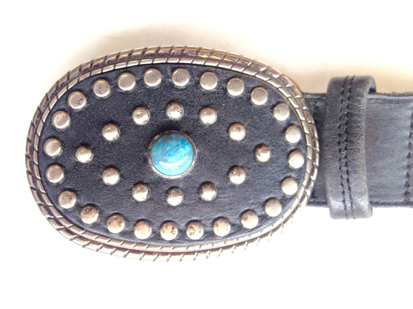 Vintage black leather belt with large oval sterling silver buckle featuring turquoise center stone and decorative silver studs around the border of the buckle.