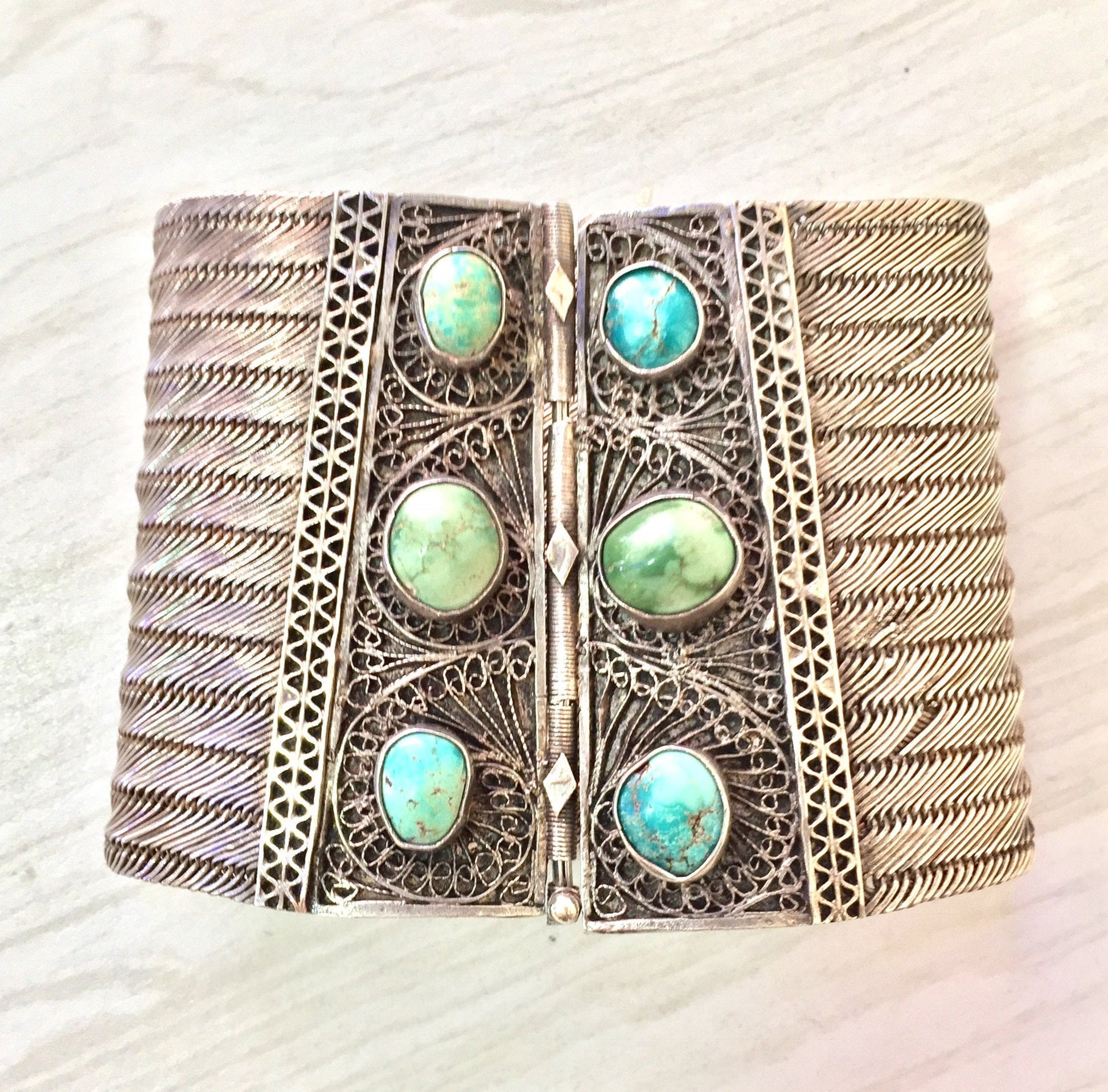 Antique silver filigree cuff bracelet with six round turquoise cabochons arranged in two vertical rows, set against an intricately etched silver bracelet with a woven pattern resembling ropes or chains. The bracelet has a substantial, bold look suitable for making a statement.