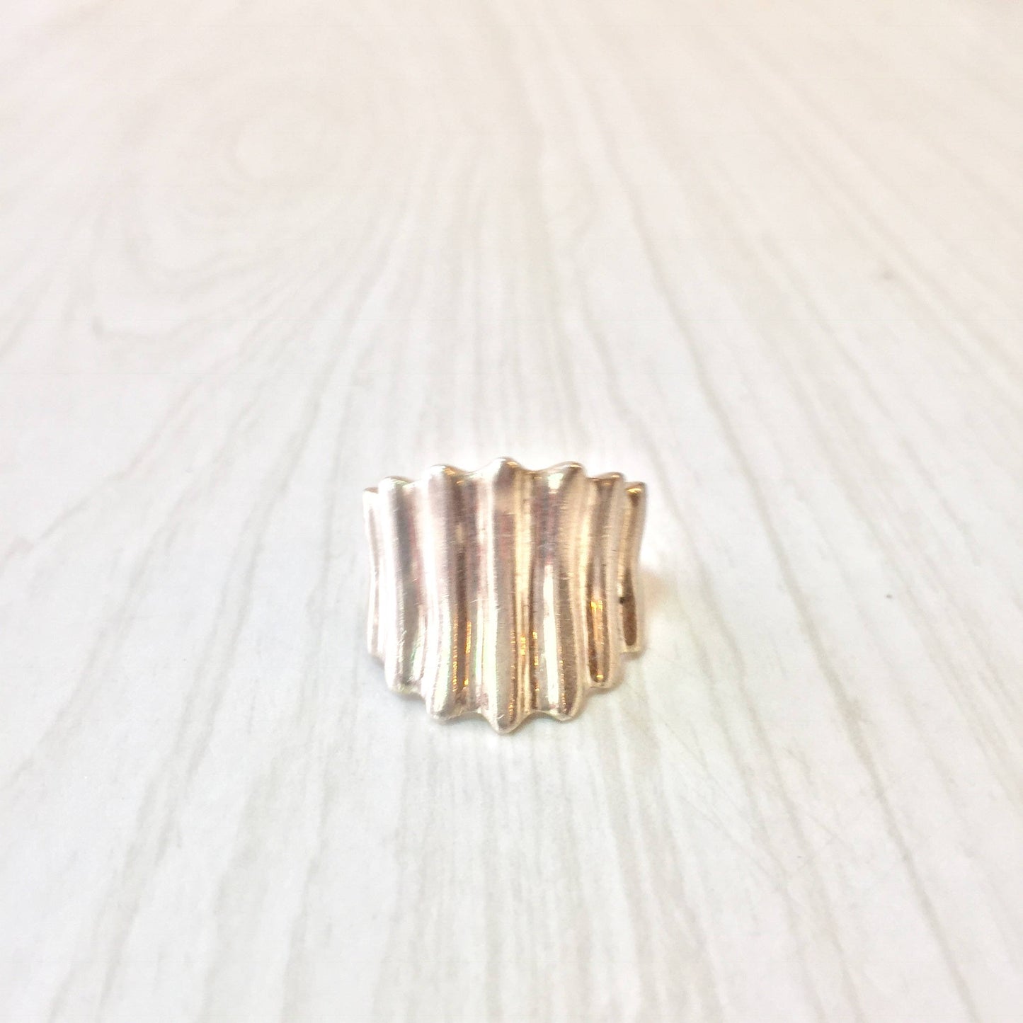 Textured sterling silver concave ring on light wood surface, minimalist unisex jewelry design