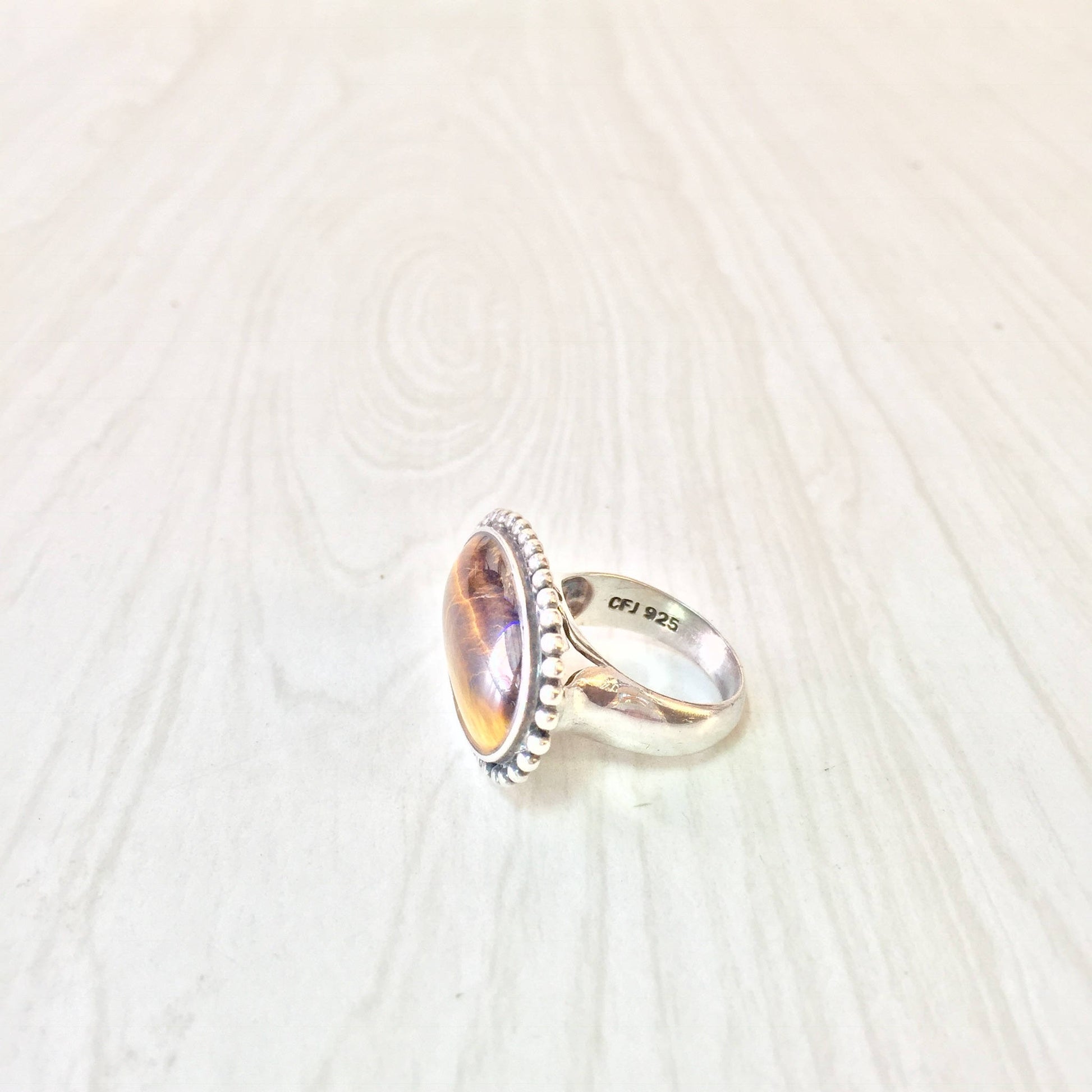 Vintage sterling silver ring with an oval-shaped tiger's eye gemstone, displayed on a light wooden surface.