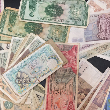 A collection of vintage foreign paper currency from various countries, featuring different denominations and colorful designs, arranged in a scattered overlapping pattern for scrapbooking or craft projects.