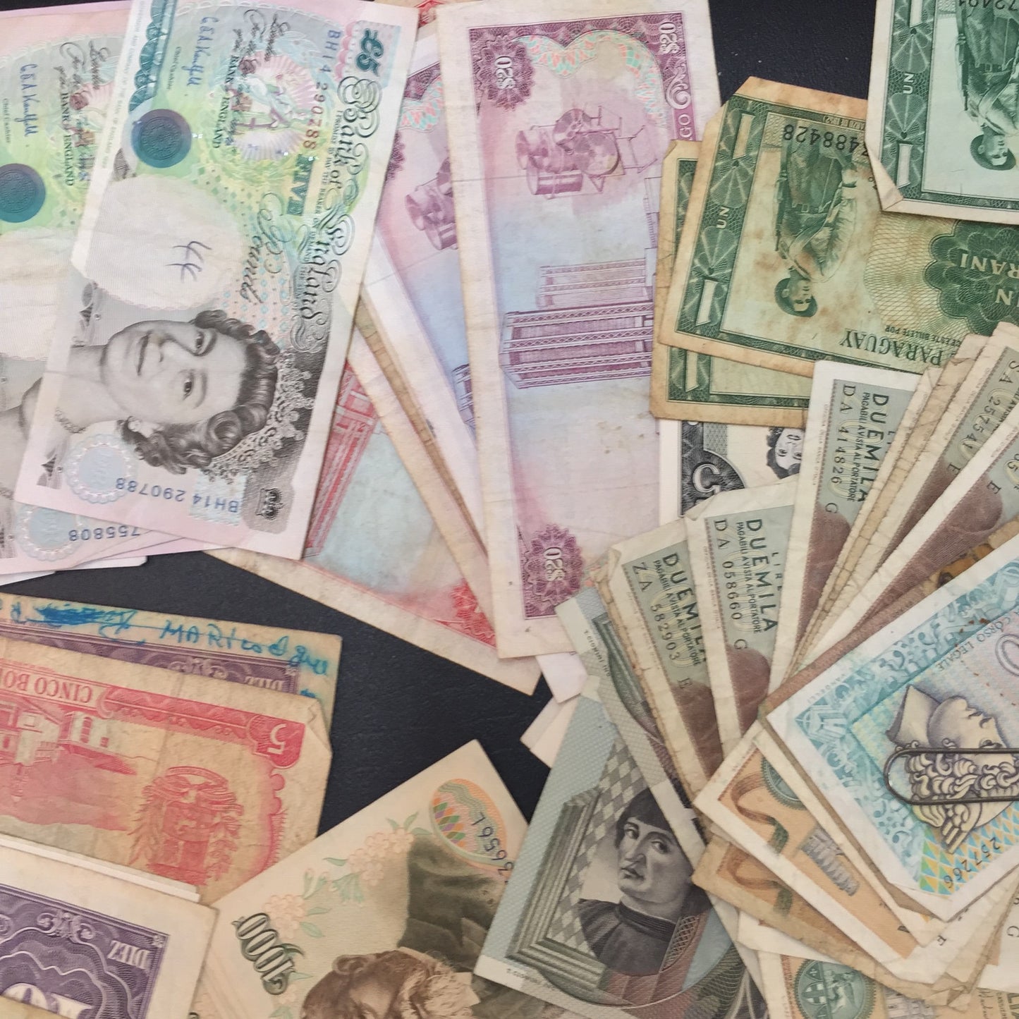 Vintage foreign currency banknotes from various countries scattered on a surface, including colorful bills featuring portraits and architectural designs, suitable for scrapbooking, crafting or collecting old paper money.