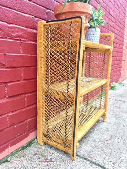 Wicker shelf unit with three shelves leaning against a red brick wall, providing decorative storage solution for a bohemian or eclectic home decor style.