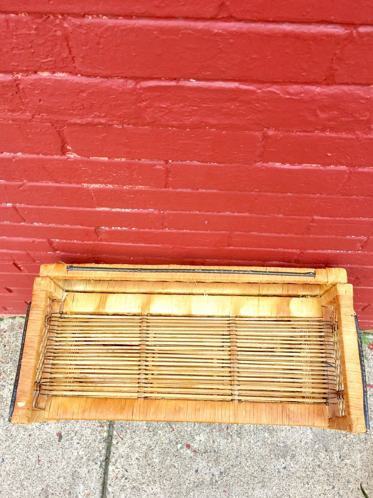 Woven wicker shelving unit in front of red brick wall, bohemian home decor storage solution