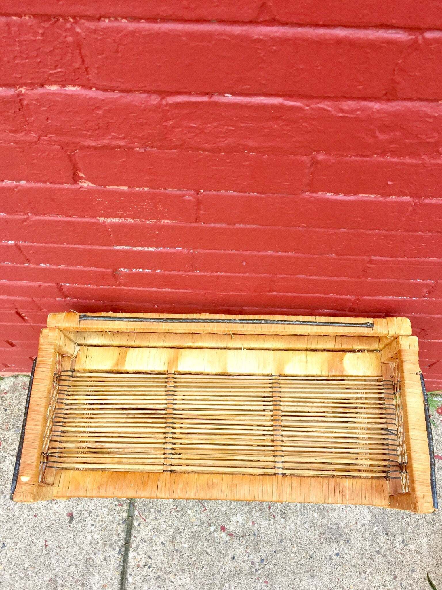 Woven wicker shelving unit in front of red brick wall, bohemian home decor storage solution