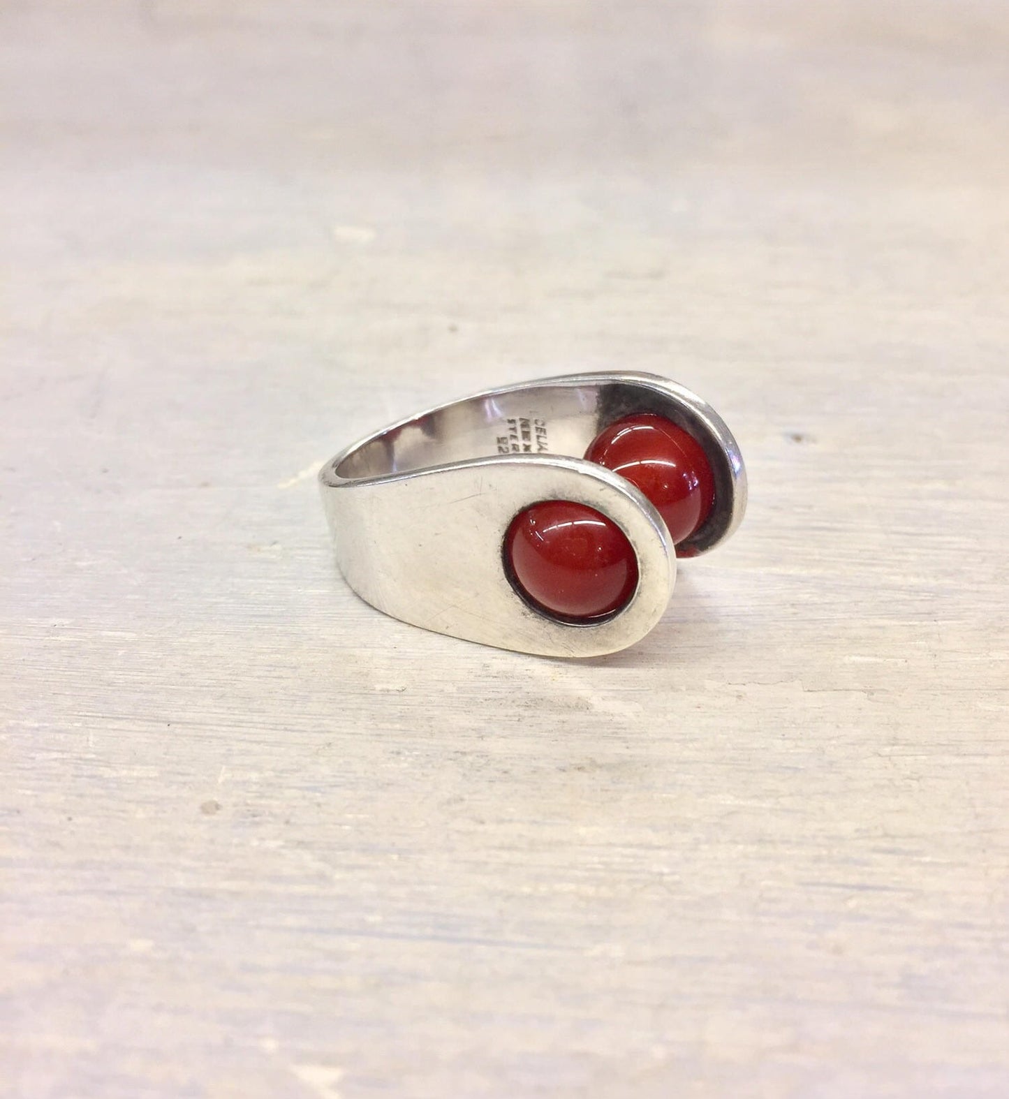 Sterling silver ring with two round red carnelian cabochon stones set in a curved bezel on a textured silver band, photographed on a light background.