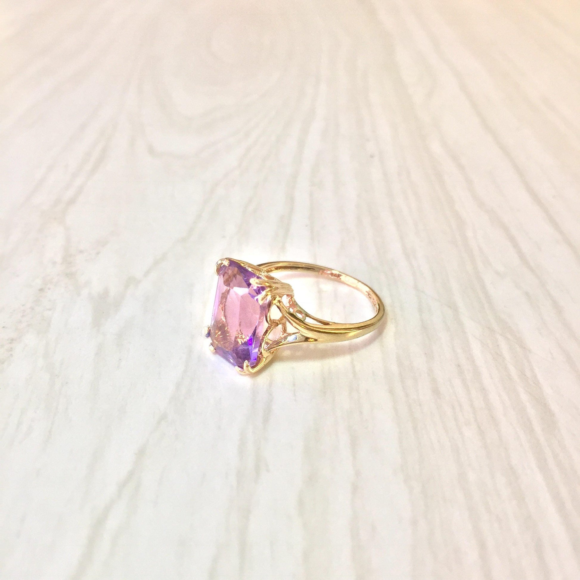 14 karat gold ring with an emerald cut amethyst gemstone on a light colored textured background