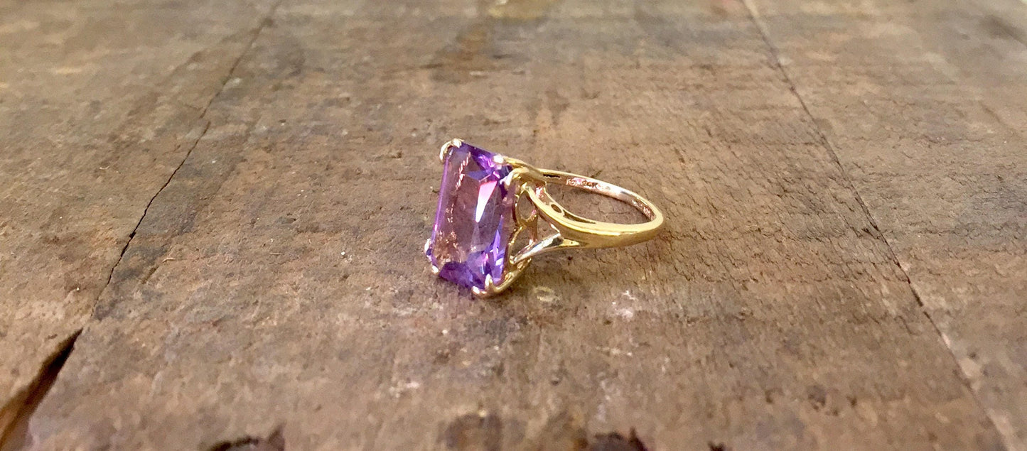 14 karat gold ring with an emerald cut amethyst stone on a wooden surface