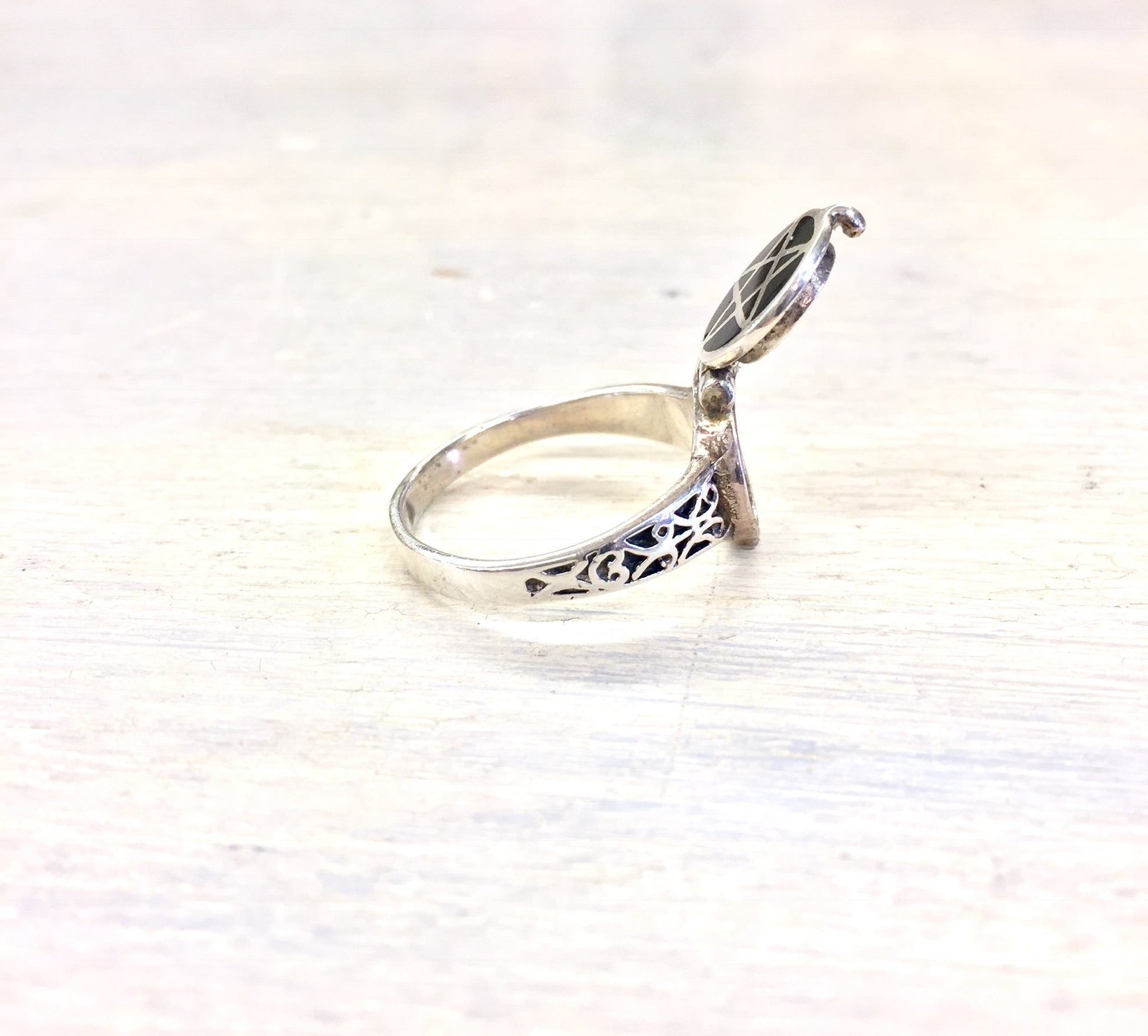 Sterling silver poison ring with floral filigree design and hinged lid, displayed on white wooden surface.