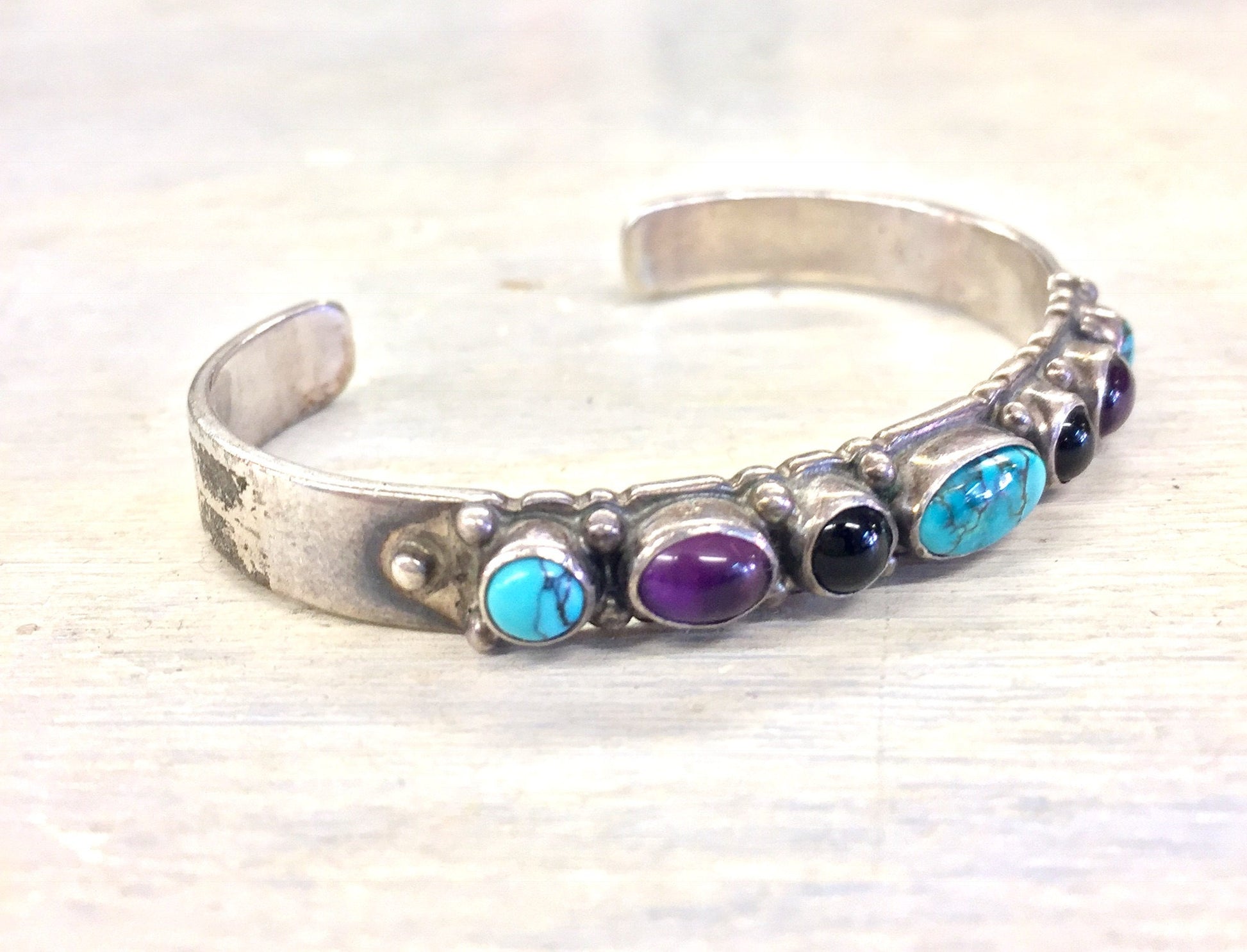 Sterling silver cuff bracelet with turquoise, onyx and purple gemstones on a textured background