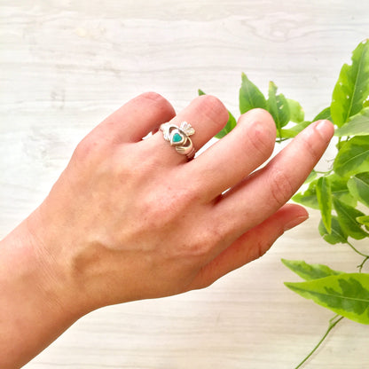 Sterling silver Claddagh ring with blue aqua stone held in front of green leaves, displaying the traditional Irish symbol of love, loyalty and friendship on a hand.