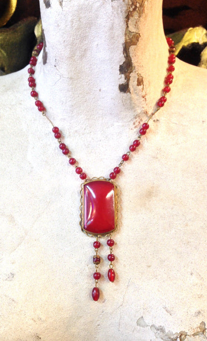 Vintage red beaded necklace with gothic pendant on weathered stone surface