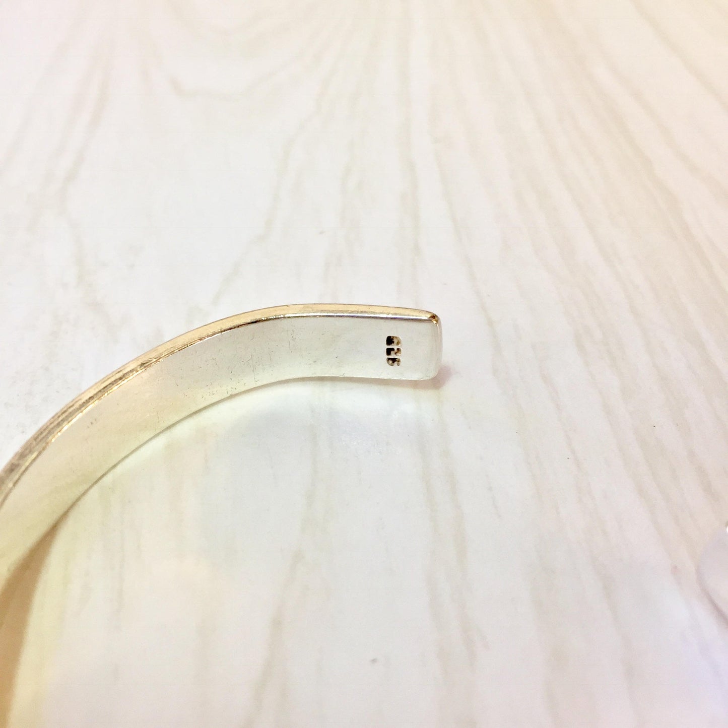 Simple twist sterling silver cuff bracelet with minimalist design on light wooden surface