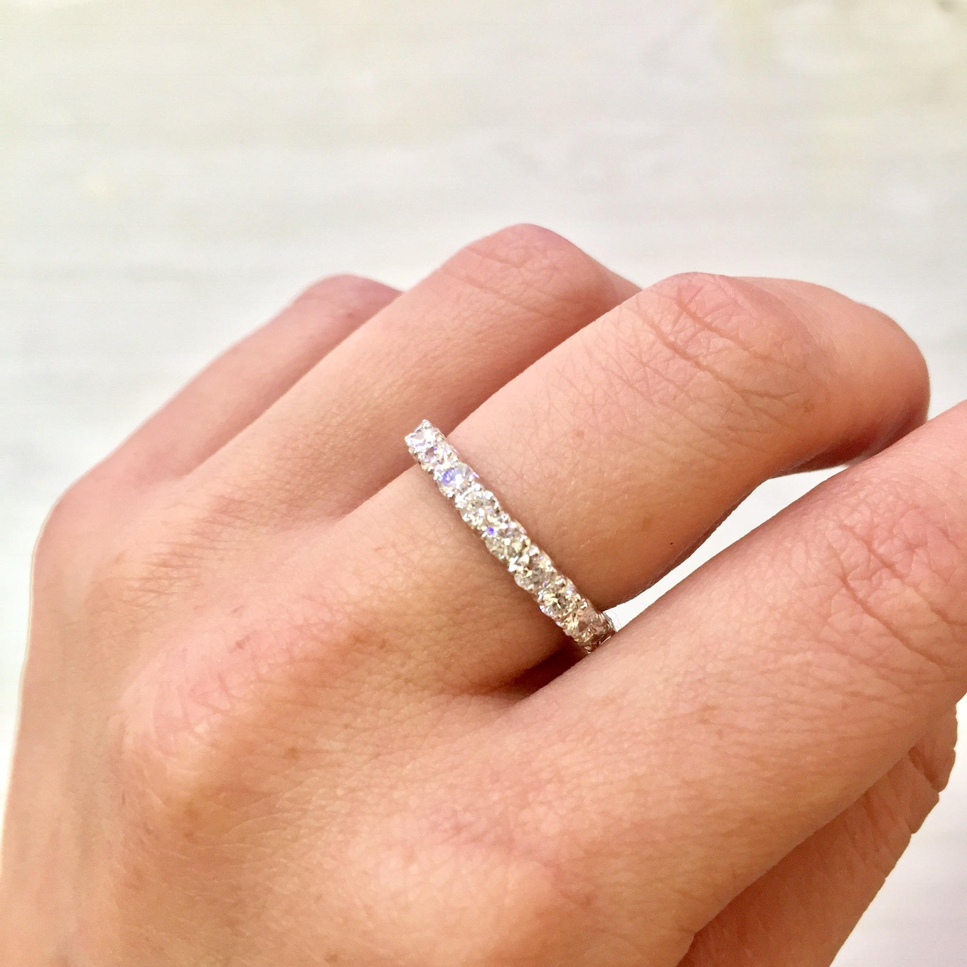 14 karat white gold and diamond wedding band on a finger, showcasing an eternity ring design with small round diamonds encircling the entire band.