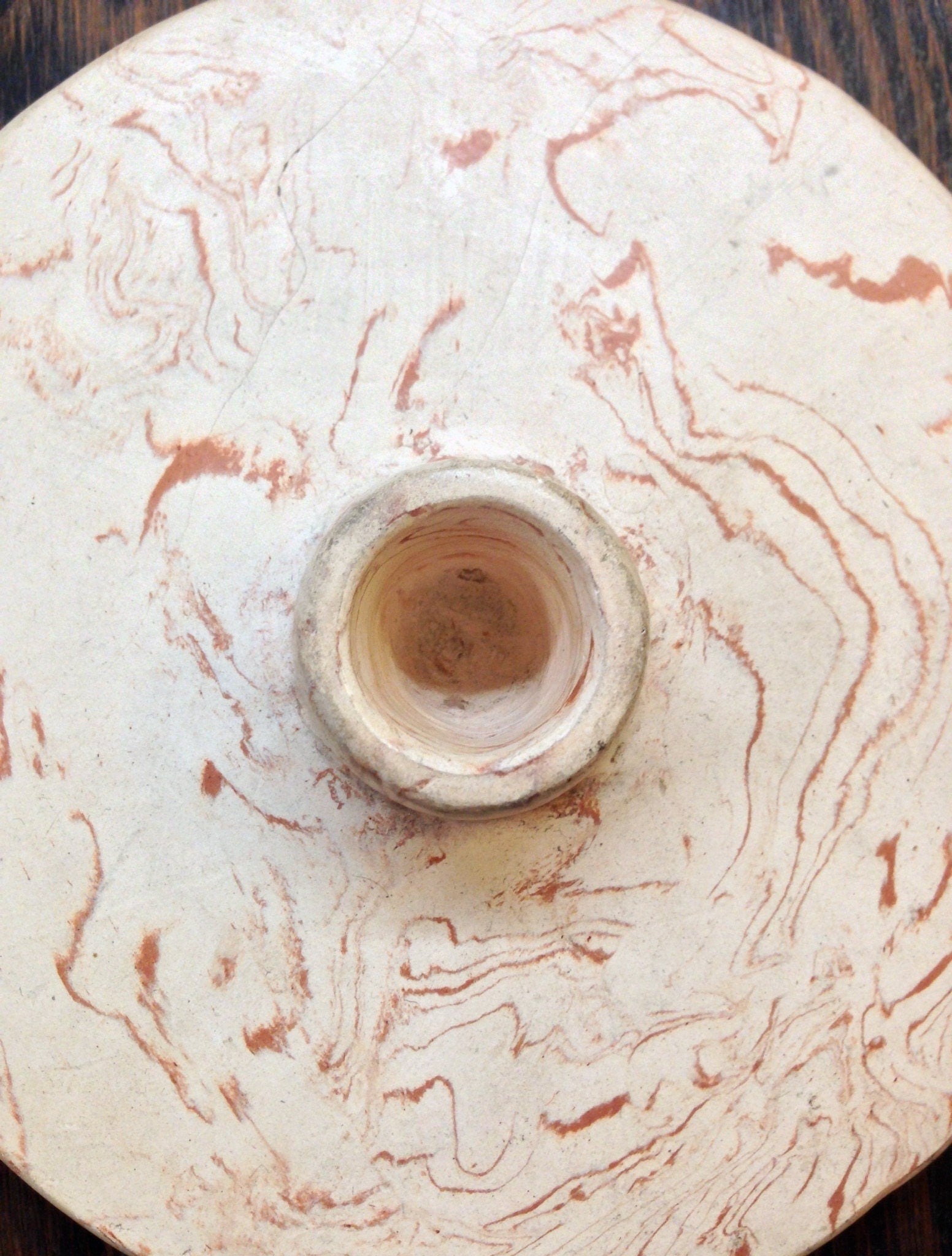 Antique ceramic tobacco pipe with swirled gray and tan clay and a circular opening, viewed from above on a wooden surface