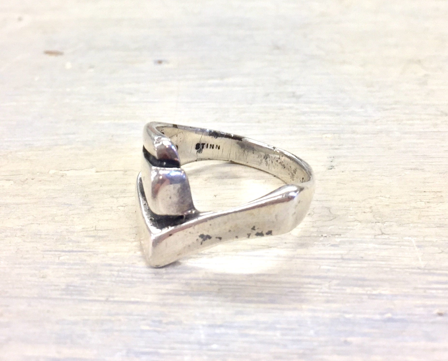 Vintage sterling silver wishbone-shaped ring with bent design on textured white wood surface