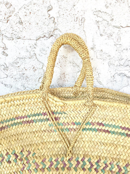 Handwoven straw beach bag with colorful striped pattern and rounded handles against a textured white background