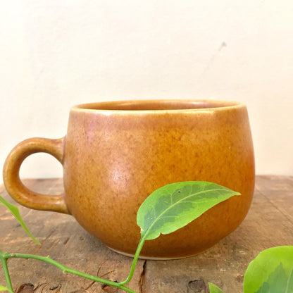 Vintage brown stoneware mug with green leaf on rustic wooden surface