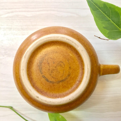 Ceramic mug with brown and tan swirled glaze on white background with green leaves