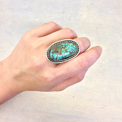 Vintage silver ring featuring a large oval turquoise stone in a bezel setting, held in a hand against a light background