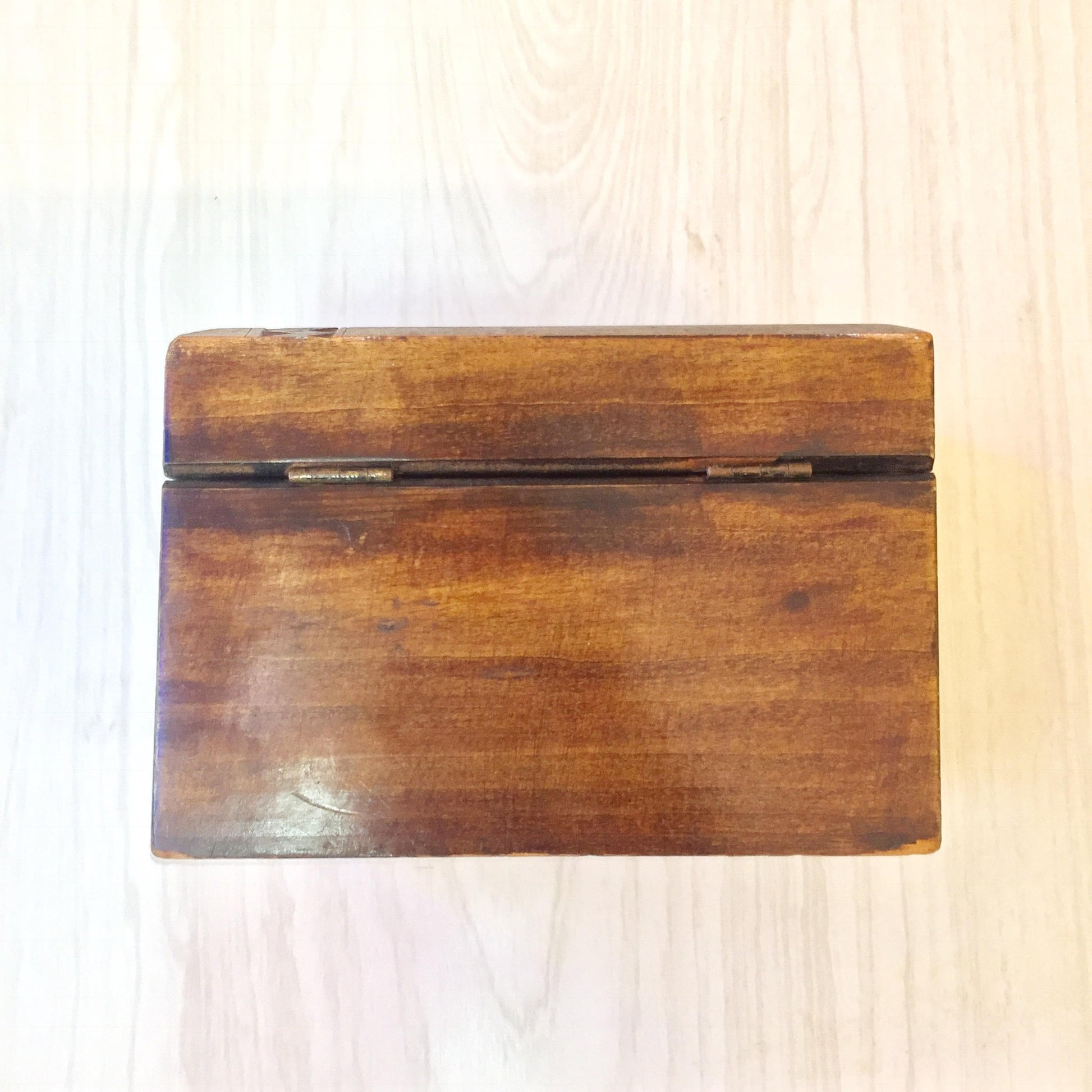 Antique wooden box with hinged lid, hand carved from darkened wood with smooth finish and natural wood grain texture visible, photographed on light wood background