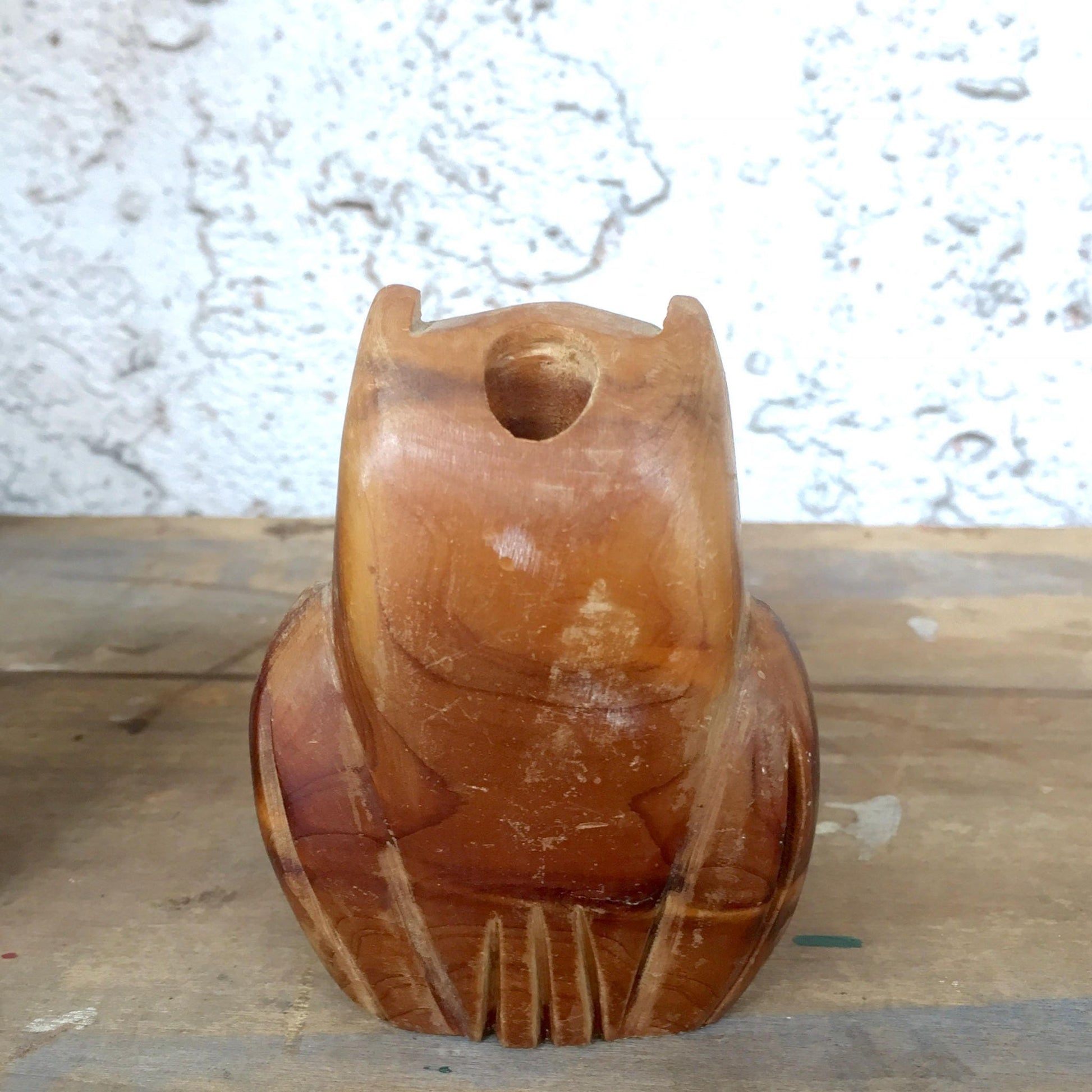 Vintage hand-carved wooden owl figurine with a hollow center, serving as a rustic pencil holder or desk organizer. The owl has a rounded shape with incised details resembling feathers and large circular eyes. The warm brown wood tones show natural grain and weathering. Positioned on a wooden surface against a textured white background.