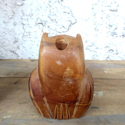 Vintage hand-carved wooden owl figurine with a hollow center, serving as a rustic pencil holder or desk organizer. The owl has a rounded shape with incised details resembling feathers and large circular eyes. The warm brown wood tones show natural grain and weathering. Positioned on a wooden surface against a textured white background.