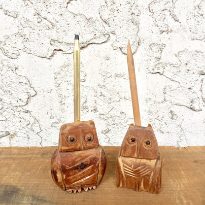 Two vintage wooden owl carvings used as pencil holders, sitting on a wooden surface against a textured white background.