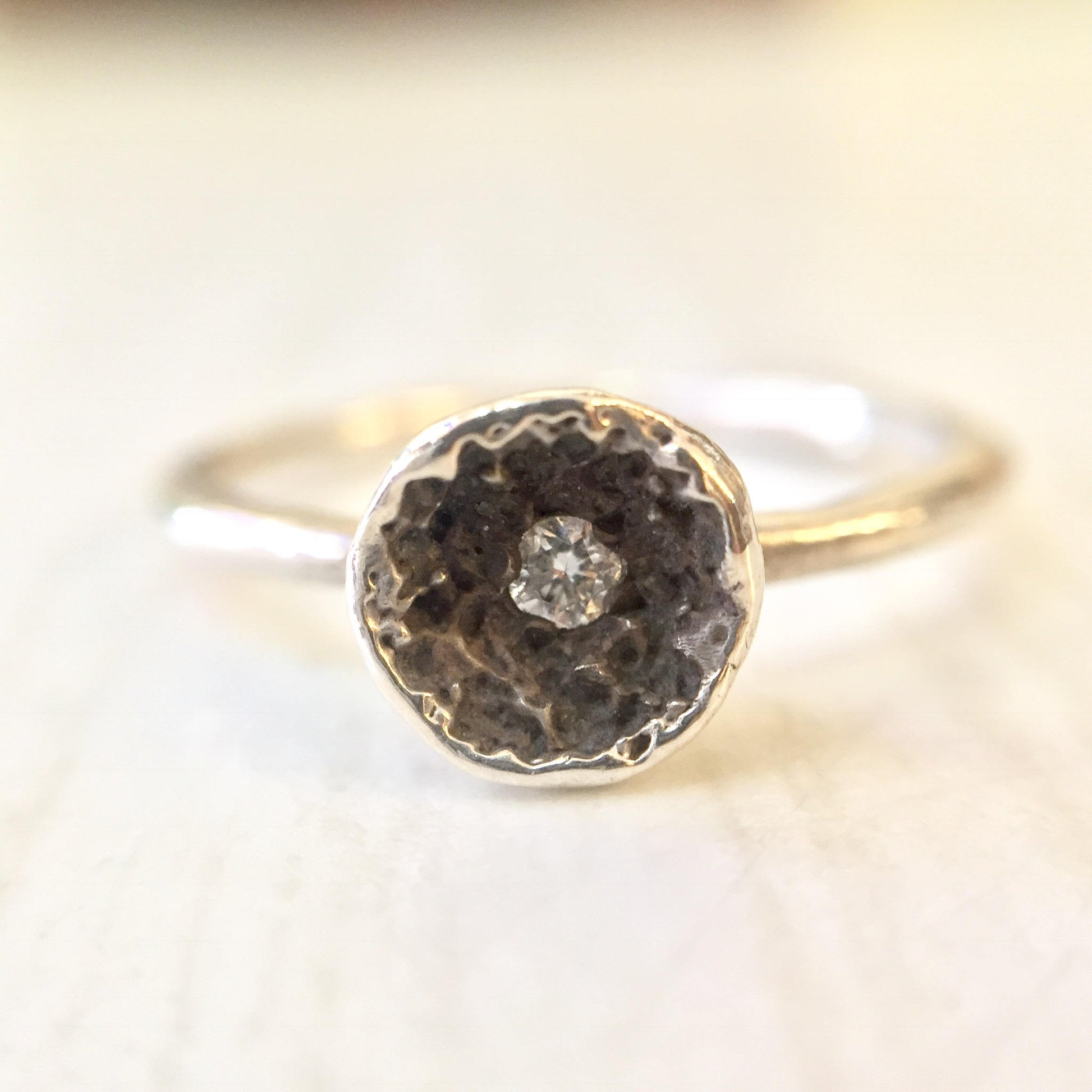 Sterling silver ring featuring a round diamond solitaire set in a hammered dome design, shown on a light textured background