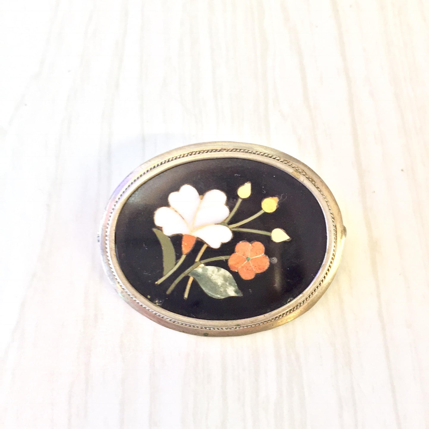 Sterling silver oval brooch pin with inlaid natural stones depicting a floral design against a dark background