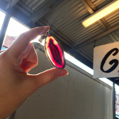 Sterling silver pendant featuring a large, oval-shaped purple agate stone, held up in front of a bright window in a warehouse or garage setting with corrugated metal roof.