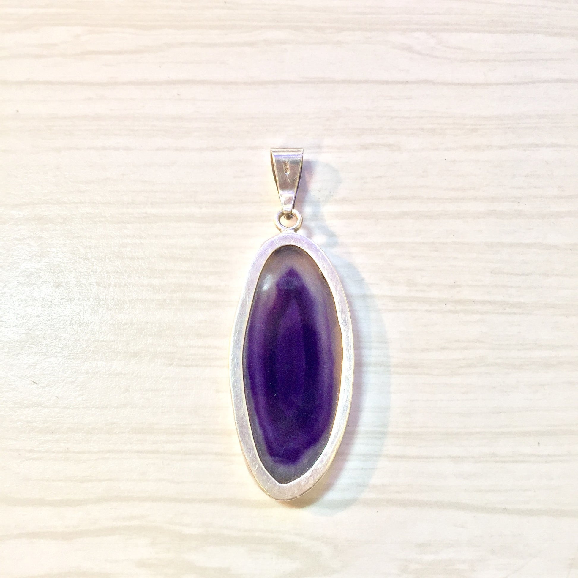 Sterling silver pendant featuring a large oval-shaped purple agate gemstone, photographed on a light colored textured background.